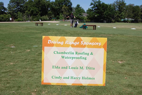 A coroplast sponsor recognition yard sign on wire stakes at an outdoor Houston event