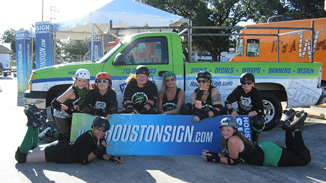 Houston Sign Company vehicles, feather flags, and a branded banner set up at a Houston community event
